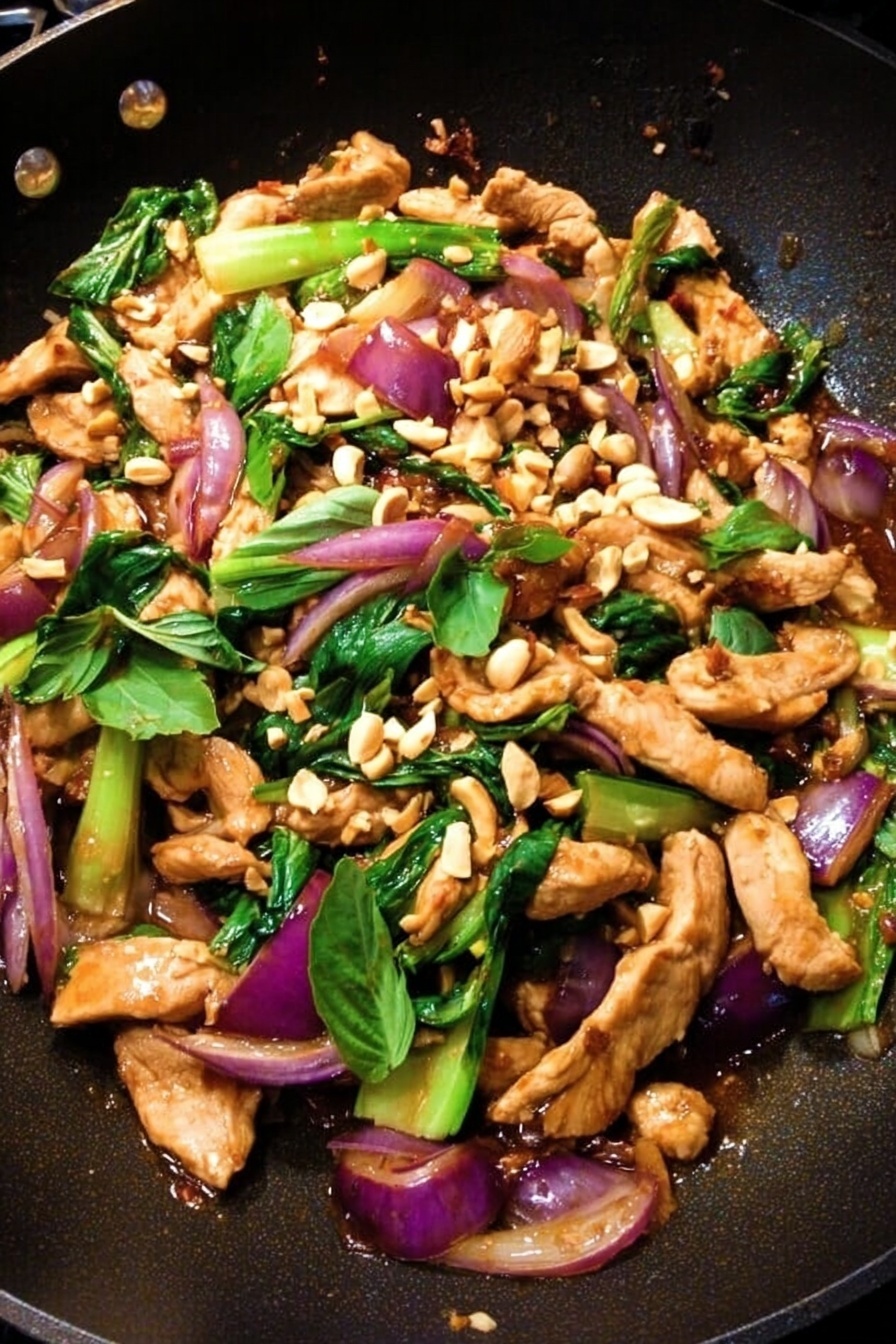 The dish is shown in a black pan filled with several layers: the bottom layer is dark brown sauce with a glossy texture, evenly spread. On top of that are long, light brown cooked chicken strips scattered around. Mixed among the chicken are chopped green bok choy pieces with a shiny, fresh texture. There are also slices of reddish-purple cooked onion adding color contrast. Fresh green basil leaves are sprinkled throughout, enhancing the look with their bright green color. Finally, chopped peanuts are spread on top, adding a crunchy texture and light tan color. photo taken with an iphone --ar 2:3 --v 7