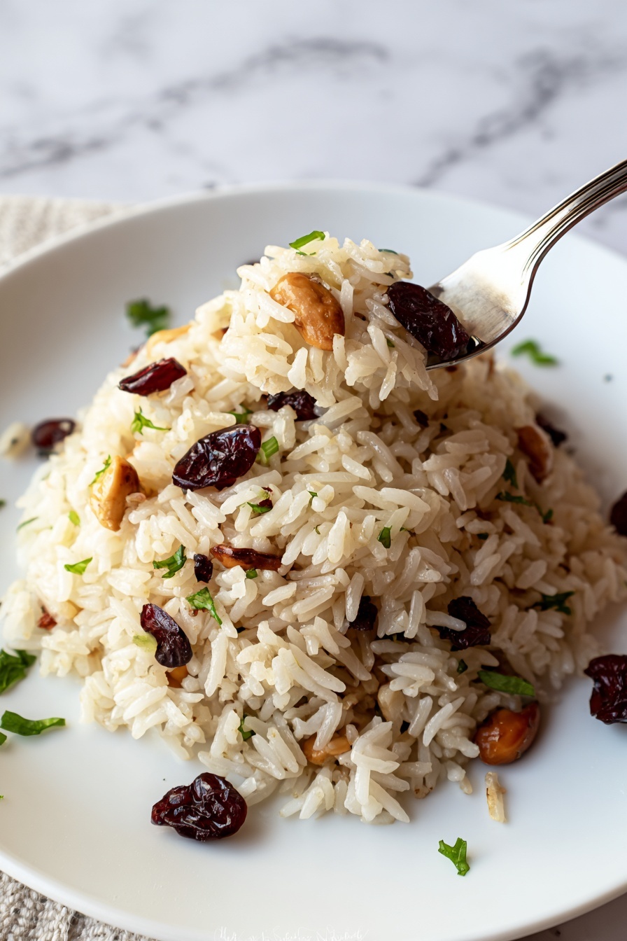 A white plate holds a single layer of rice pilaf mixed with crimson dried cranberries and light brown sliced almonds, with small bits of green herbs scattered on and around the rice. The pilaf is clumped in the center, showing the shiny and slightly separated grains of rice with bits of nuts and fruit evenly spread throughout. The background features a white marbled texture, and part of a silver fork is visible at the left edge of the plate. photo taken with an iphone --ar 2:3 --v 7