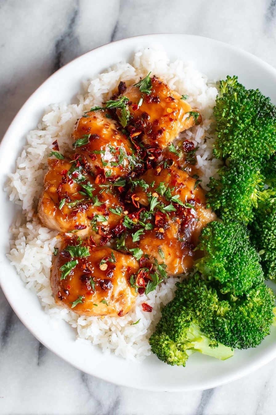 A white plate holds a meal with three layers: the bottom layer is white steamed rice with soft, grainy texture; on top are several pieces of glazed chicken coated with a shiny, dark reddish-brown sauce sprinkled with green chopped herbs and tiny red chili flakes; on one side of the plate, bright green and fresh broccoli florets add a crunchy texture and vibrant contrast. The plate is on a white marbled surface. photo taken with an iphone --ar 2:3 --v 7