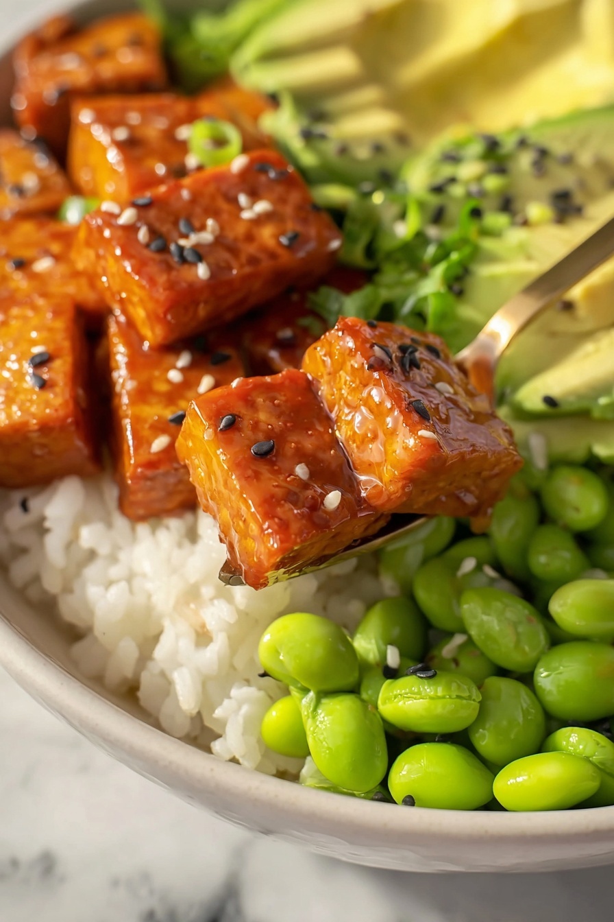 The image shows a close-up of a white bowl filled with four layers of food. At the bottom is a bed of white rice with a soft texture. On top of the rice, there are bright green edamame beans, shiny and smooth. Next to the edamame is a layer of sliced avocado, light green with a creamy look, sprinkled with black and white sesame seeds. Above the avocado and edamame are square pieces of glazed tempeh, a rich orange-brown color and shiny from the sauce, also sprinkled with black and white sesame seeds and small pieces of chopped green onions. A golden spoon holds two pieces of tempeh above the bowl. The whole scene is set on a white marbled surface. Photo taken with an iphone --ar 2:3 --v 7