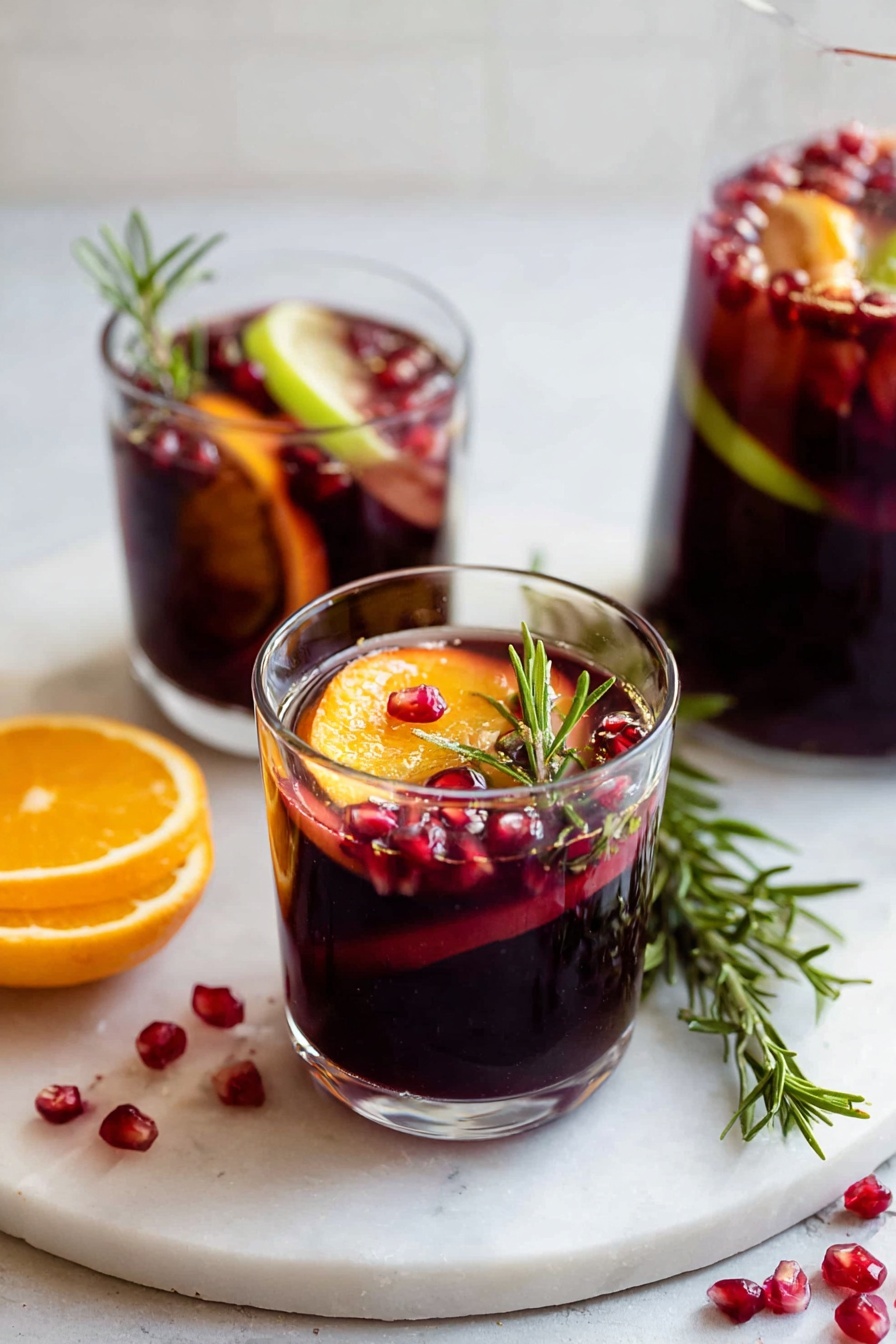 Two clear glass cups sit on a white marbled surface, each filled with a deep red liquid. Inside each cup, visible layers include bright orange slices, thin light green apple slices, and scattered dark red pomegranate seeds floating throughout. A sprig of green rosemary stands upright in the closest cup, adding texture and height. Around the glasses, red pomegranate seeds are scattered on the marbled surface, and a small bunch of fresh rosemary lies nearby. The background is softly blurred with a clean white tone. photo taken with an iphone --ar 2:3 --v 7