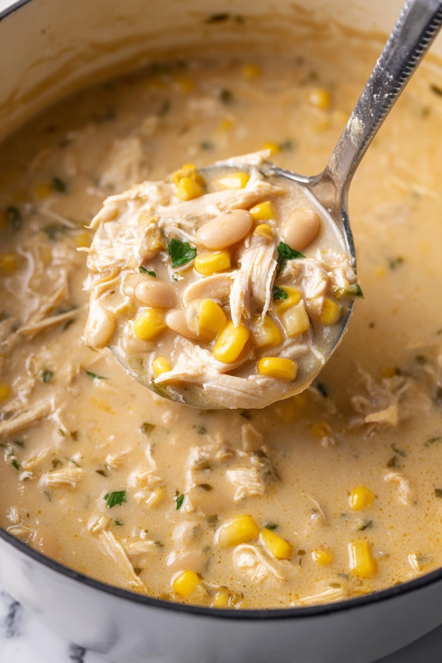 The image shows a close-up of a thick, creamy soup inside a large white pot with a silver ladle lifting some of the soup. The soup has a light beige color with visible yellow corn kernels, white beans, and shredded white chicken mixed throughout. Small green herb pieces are scattered in the soup, adding contrast. The soup’s texture looks smooth and rich with chunky pieces evenly spread in the creamy base. The photo is taken over a white marbled surface. photo taken with an iphone --ar 2:3 --v 7