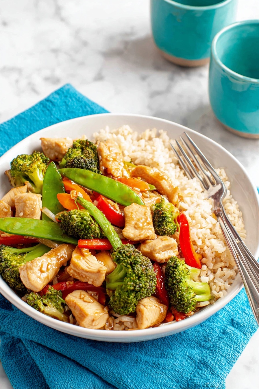 A white plate sits on a white marbled surface with a turquoise napkin underneath. The plate holds three layers: the bottom layer is light brown cooked rice with a soft, fluffy texture; the middle layer consists of bright green snow peas and fresh broccoli florets with a slightly charred look; the top layer has pieces of light golden cooked chicken, thin orange carrot strips, and slices of red bell pepper, all mixed and glistening lightly. Two silver forks rest on the right side of the plate. In the background, there are two turquoise ceramic cups. Photo taken with an iphone --ar 2:3 --v 7