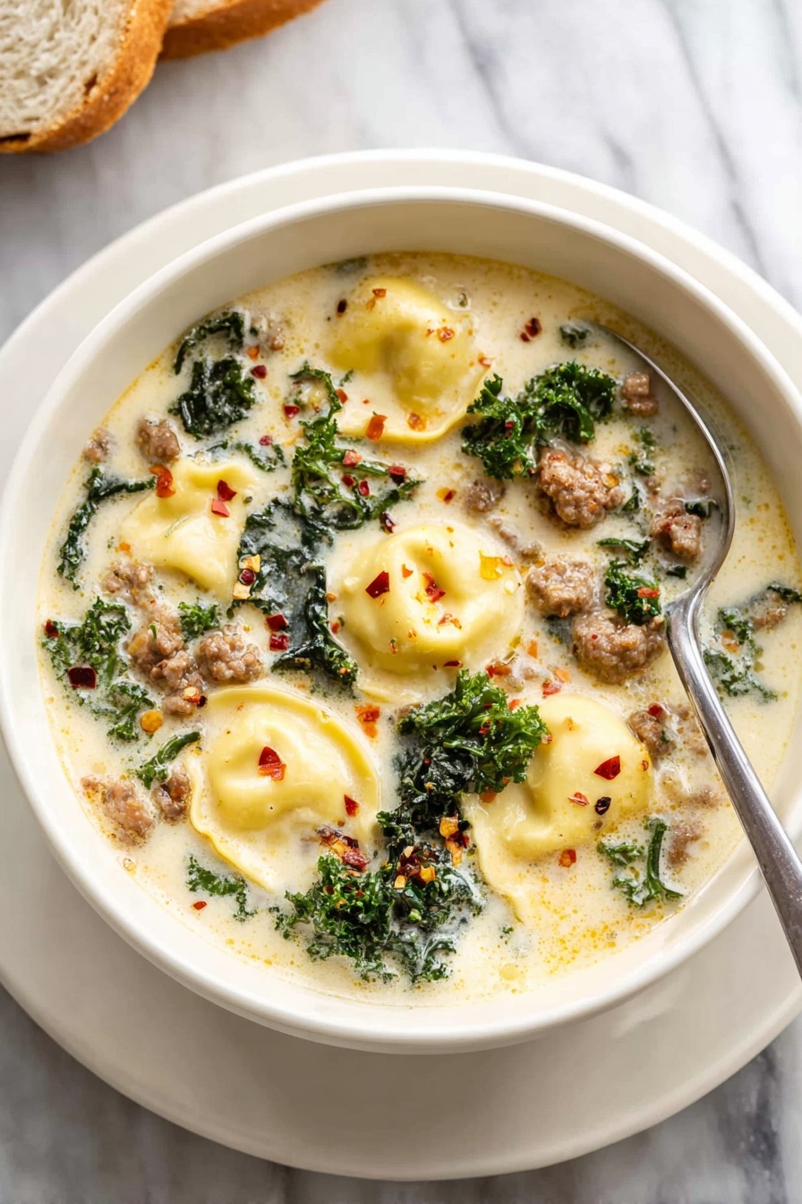 The image shows a white bowl filled with creamy soup placed on a white marbled surface. The soup has four visible layers of ingredients: at the top and mostly floating are four large yellow tortellini pasta pieces with soft, smooth texture. Mixed throughout the creamy light beige soup are small chunks of browned ground meat with a slightly crumbly texture and deep brown color. Bright green leafy kale pieces are scattered throughout, adding a fresh, textured look. Small red chili flakes are sprinkled lightly on the soup surface. A silver spoon rests inside the bowl on the right side. Photo taken with an iphone --ar 2:3 --v 7
